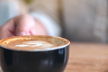 Yakından bakınca, ahşap masada bir fincan sıcak kahve tutan bir elin resmi.