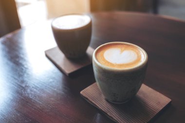 Kafedeki eski ahşap masada iki küçük fincan sütlü kahvenin yakın plan görüntüsü.