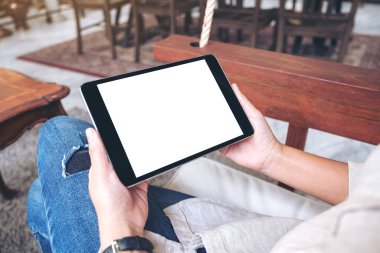 Kafede otururken siyah tableti beyaz ekranla tutan bir kadının ellerinin görüntüsü.