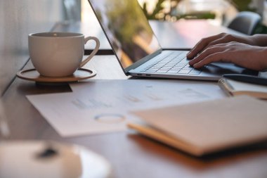 Ofisteki masanın üzerinde not defterleri ve kağıtlarla bir kadının ellerinin dizüstü bilgisayarda yazıp kullandığı yakın plan görüntüsü.