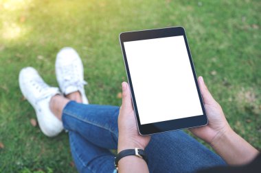 Açık havada otururken beyaz ekranlı siyah tablet tableti tutan ve kullanan bir kadının görüntüsü