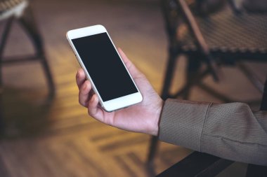 Boş siyah masaüstü ekranı ve bulanık arkaplanı olan beyaz cep telefonunu tutan bir elin görüntüsü