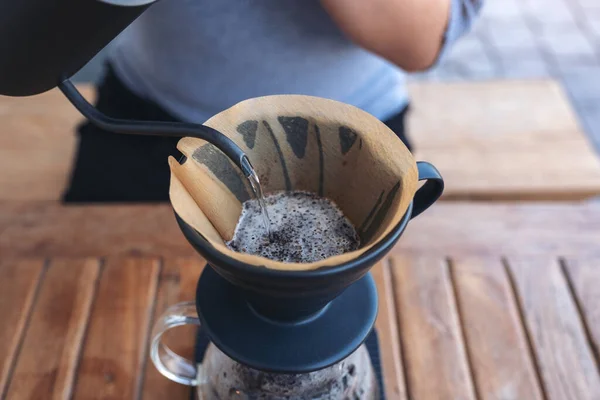 Closeup image of a woman's hand pouring hot water to make a drip coffee on vintage wooden table