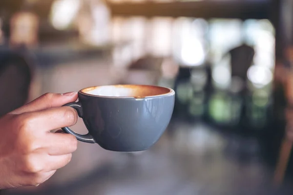 店内にはブルーのホットコーヒーを持った手のイメージが滲んでいる — ストック写真