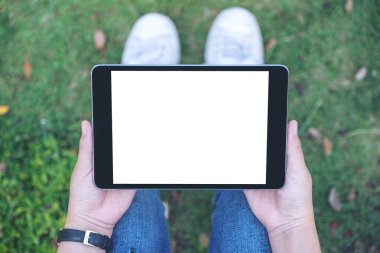 Açık havada otururken beyaz masaüstü ekranlı siyah tablet tableti tutan ve kullanan bir kadının en üstteki görüntüsü