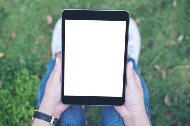 Açık havada otururken boş beyaz masaüstü ekran ile siyah tablet tableti tutan ve kullanan bir kadının en üst görünüm görüntüsü
