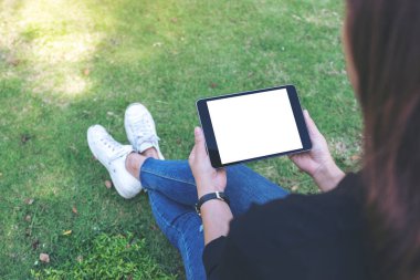 Açık havada otururken beyaz masaüstü ekranlı siyah tablet tableti tutan ve kullanan bir kadının görüntüsü