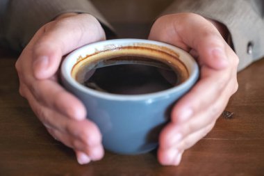 Yakından bakınca, kafedeki ahşap masada mavi bir fincan kahve tutan ellerin görüntüsü.