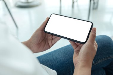 Kafedeki beyaz ekranlı, siyah cep telefonlu bir kadının ellerinin görüntüsü.