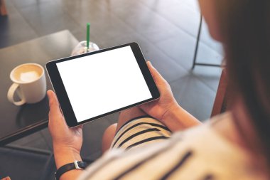 Kafede otururken elinde boş beyaz ekranlı siyah tablet tutan bir kadının görüntüsü.