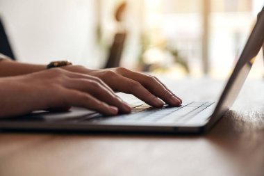 Masadaki dizüstü bilgisayarın klavyesini kullanan ve yazan kadınların ellerinin yakın plan görüntüsü.