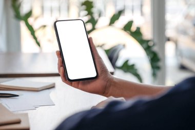 Ofiste çalışırken cep telefonunu boş ekran ile tutan ve kullanan bir kadının görüntüsü