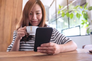 Kahve içerken elinde tutan, kullanan ve akıllı telefona bakan bir kadının yakın plan görüntüsü. 