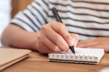 Bir kadının eli ahşap masaya boş bir defter yazarken yakın plan görüntüsü.