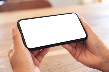 Ahşap masanın üzerinde beyaz ekranlı, siyah cep telefonlu bir kadının ellerinin görüntüsü.