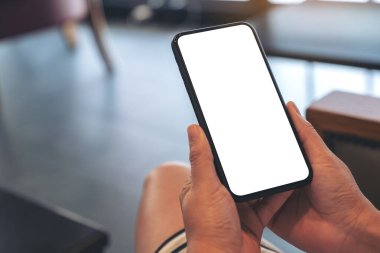 Kafedeki boş beyaz ekranlı siyah cep telefonlu bir kadının ellerinin görüntüsü.