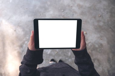 Üst görünümde, açık havada dikilirken beyaz masaüstü ekranlı siyah tablet tableti kullanan kadınların ellerinin görüntüsü var.