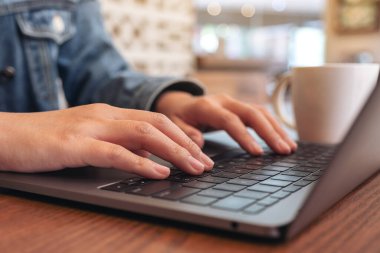 Laptop bilgisayarının klavyesinde kahve bardağını kullanan ve daktilo kullanan kadınların yakın çekim görüntüleri.