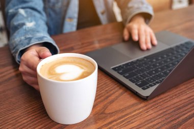 Bir kadının, kahve içerken laptopta dokunduğu ve dokunduğu yakın plan görüntüsü.