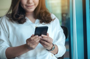 Kafede elinde tutan, kullanan ve akıllı telefona bakan bir kadının yakın plan görüntüsü.