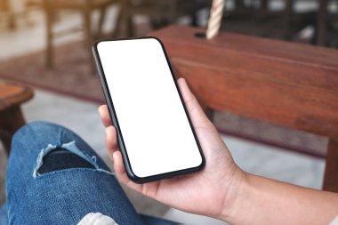 Kafede otururken siyah cep telefonunu beyaz ekran ile tutan ellerin görüntüsü