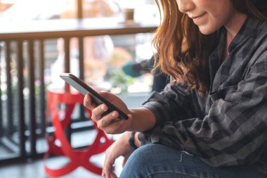 Kafede elinde tutan, kullanan ve akıllı telefona bakan bir kadının yakın plan görüntüsü.