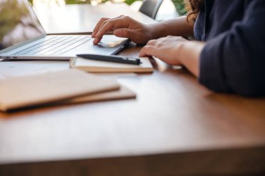 Ofisteki masanın üzerinde not defterleri ve kağıtlarla bilgisayara dokunan ve kullanan bir elin yakın plan resmi.