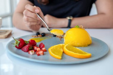 Kafede kaşık kaşık portakallı kek yiyen bir kadın.