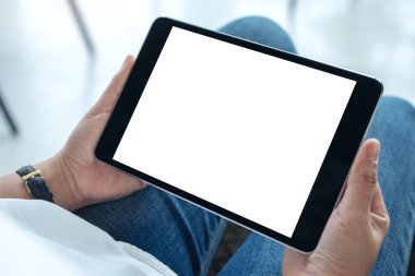 Kafede otururken elinde boş beyaz ekranlı siyah tablet tutan bir kadının görüntüsü.