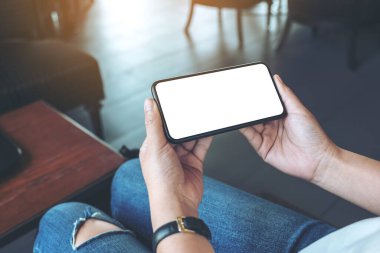 Kafedeki beyaz ekranlı, siyah cep telefonlu bir kadının ellerinin görüntüsü.