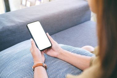 Oturma odasında rahat bir şekilde otururken elinde beyaz ekranlı siyah cep telefonu olan bir kadının görüntüsü.