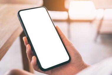 Kafedeki boş beyaz ekranlı siyah cep telefonlu bir kadının ellerinin görüntüsü.
