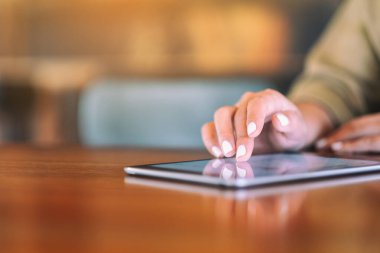 Ahşap masadaki tableti işaret eden bir kadının yakın plan görüntüsü.