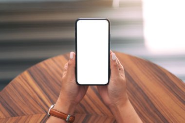 Boş beyaz masaüstü ekranlı, ahşap masa arkası olan siyah cep telefonu tutan bir kadının görüntüsü