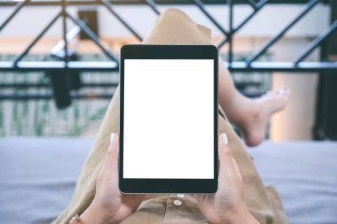 Oturma odasında uzanmış kendini rahat hissederken elinde beyaz ekranlı siyah tablet bir kadının görüntüsü.