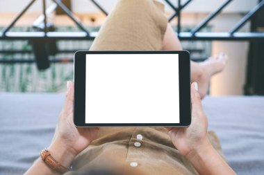 Oturma odasında uzanmış kendini rahat hissederken elinde beyaz ekranlı siyah tablet bir kadının görüntüsü.