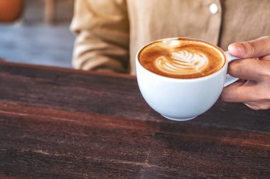 Kafe 'de bir fincan sıcak kahveyi elinde tutan bir kadının yakın plan görüntüsü.