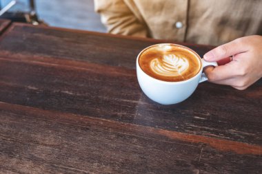 Kafe 'de bir fincan sıcak kahveyi elinde tutan bir kadının yakın plan görüntüsü.