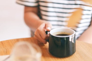 Ahşap masada elinde yeşil bir fincan kahve tutan bir kadının yakın plan görüntüsü.