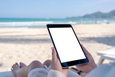 Plaj sandalyesinde uzanırken elinde boş masaüstü ekranı olan siyah bir tablet tutan bir kadının görüntüsü.