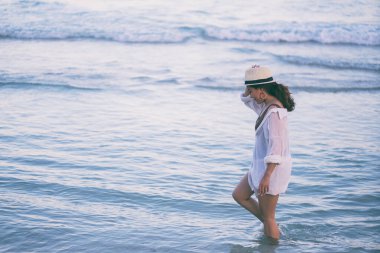 Deniz ve mavi gökyüzü arka planıyla sahilde gezinen bir kadın.