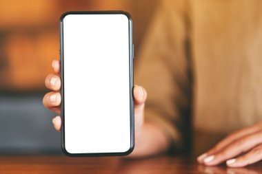 Kafedeki masada elinde siyah bir cep telefonu tutan ve gösteren beyaz ekranlı bir kadının görüntüsü.