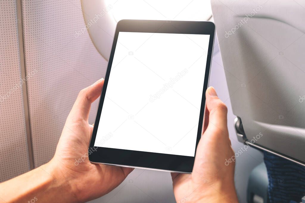 Mockup image of a man holding and looking at black tablet pc with blank white desktop screen next to an airplane window 