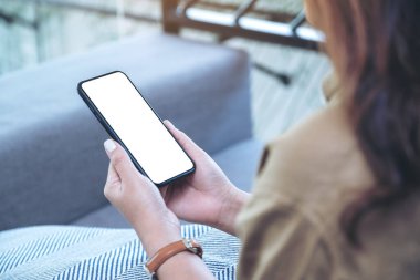 Oturma odasında rahat bir şekilde otururken elinde beyaz ekranlı siyah cep telefonu olan bir kadının görüntüsü.