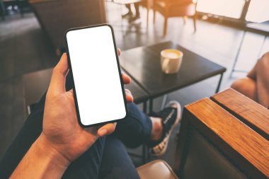 Kafedeki masada bir fincan kahve ve boş ekran ile siyah cep telefonu tutan bir adamın görüntüsü.