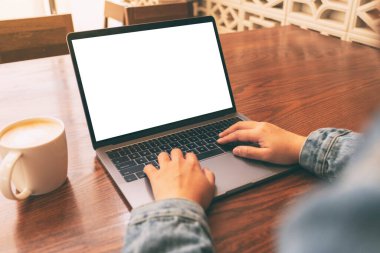 Laptop 'ta beyaz ekran ve tahta masada kahve fincanı kullanan ve daktilo kullanan bir kadının görüntüsü.