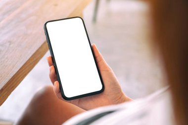 Kafede elinde siyah cep telefonu olan beyaz ekranlı bir kadının görüntüsü.