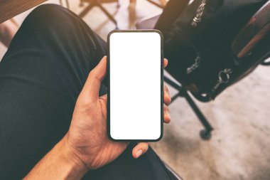 Kafedeki masada bir fincan kahve ve boş ekran ile siyah cep telefonu tutan bir adamın görüntüsü.