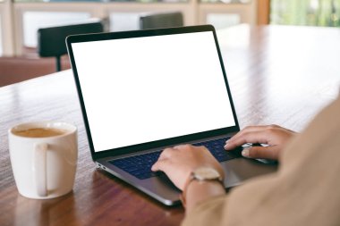Laptop 'ta beyaz ekran ve tahta masada kahve fincanı kullanan ve daktilo kullanan bir kadının görüntüsü.