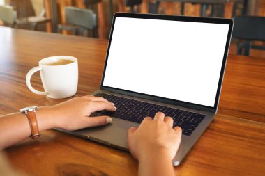 Laptop 'ta beyaz ekran ve tahta masada kahve fincanı kullanan ve daktilo kullanan bir kadının görüntüsü.